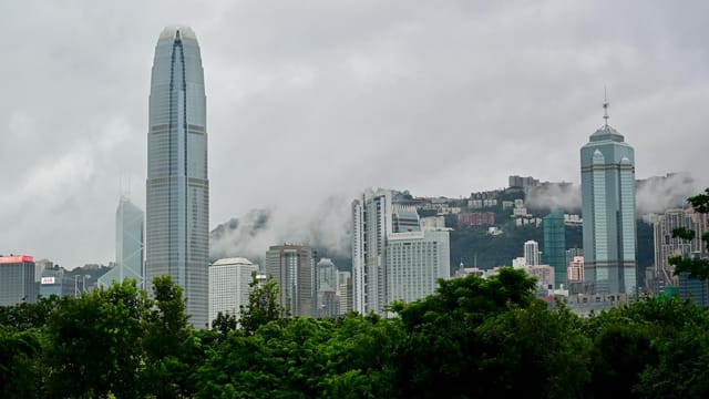 Majestic skyline of Hong Kong with fog enveloping iconic skyscrapers and lush greenery in foreground.
