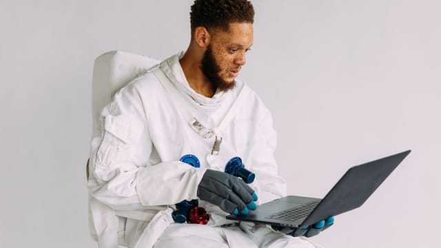 An astronaut in a space suit operating a laptop indoors, conveying technological themes.