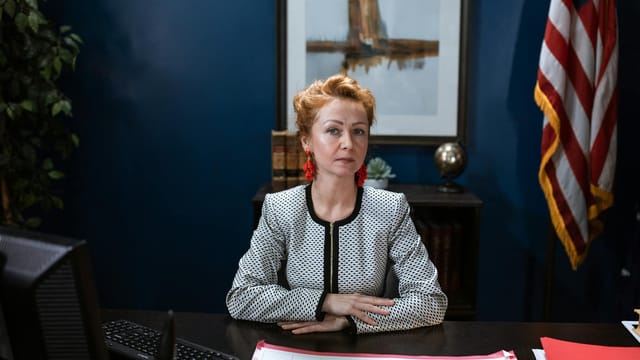 Confident woman in an office setting with a US flag behind her.