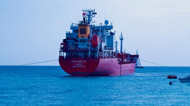 A red cargo ship sails in the calm blue ocean under a clear sky.