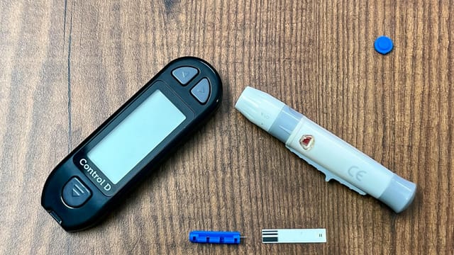 Close-up of a diabetes monitoring kit with glucometer and lancing device on a wooden surface.