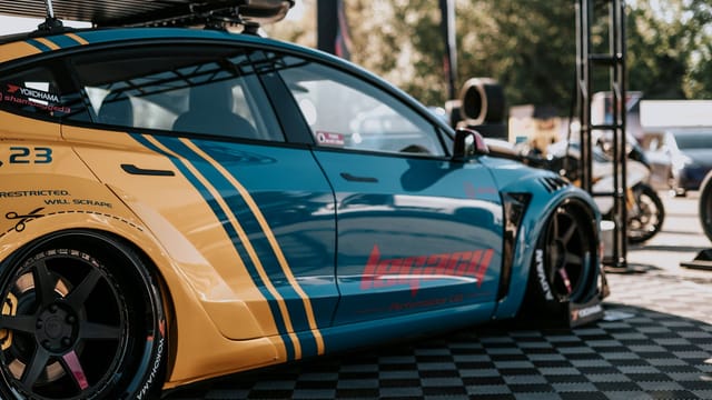 Custom blue and yellow racing car displayed at an outdoor auto show event.