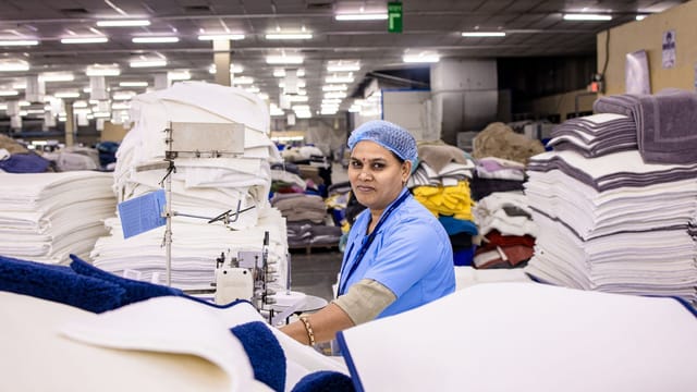 Female textile worker sewing in a busy factory. High quality production environment.