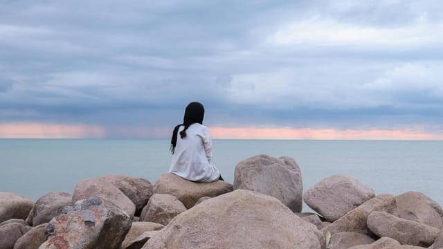 Woman in white sits on rocks overlooking the sea at Nowshahr, under a dramatic cloudy sky.