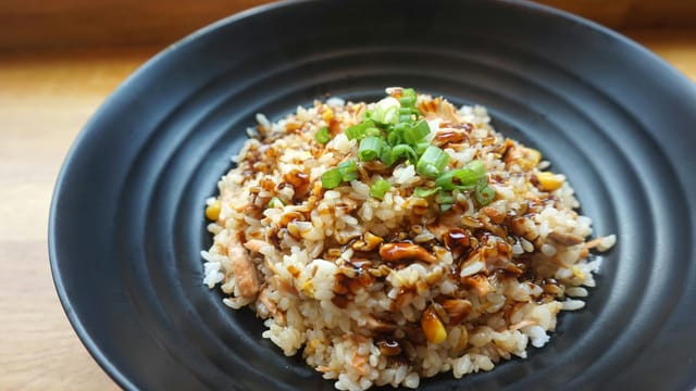 Delicious homemade fried rice with scallions and sauce on a black plate.