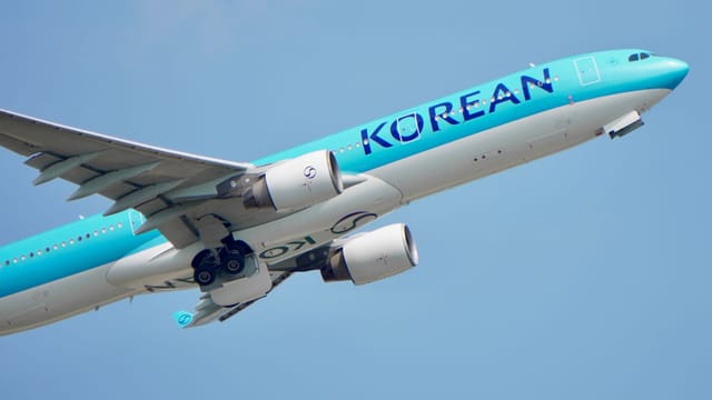 A commercial airplane with 'Korean' signage, flying against a clear blue sky.