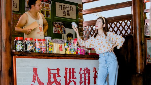 A young woman interacts with a traditional street vendor in an outdoor market setting.