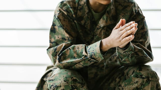 A close-up view of a soldier sitting in a camouflage uniform with clasped hands.