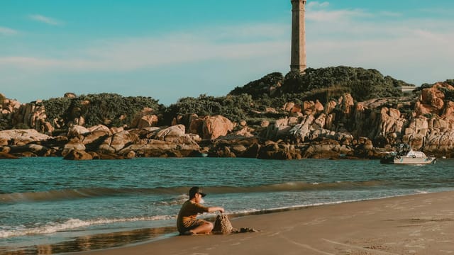 A child building sandcastles on Ke Ga Cape beach with a lighthouse in the background, Phan Thiết, Vietnam.