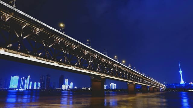 Illuminated view of Wuhan's Yangtze River Bridge with city skyline at night.