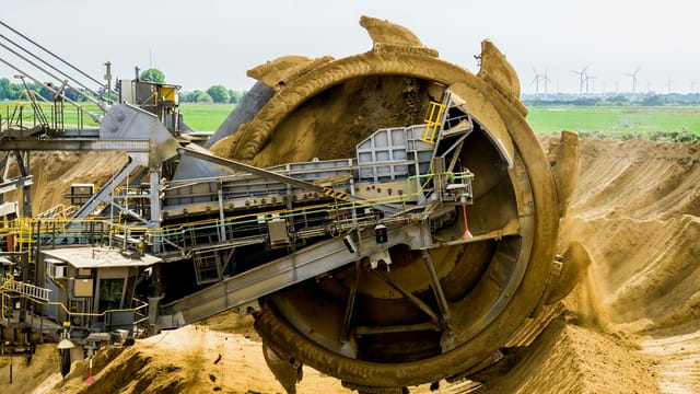A large bucket wheel excavator working in an open pit mine against a green landscape.