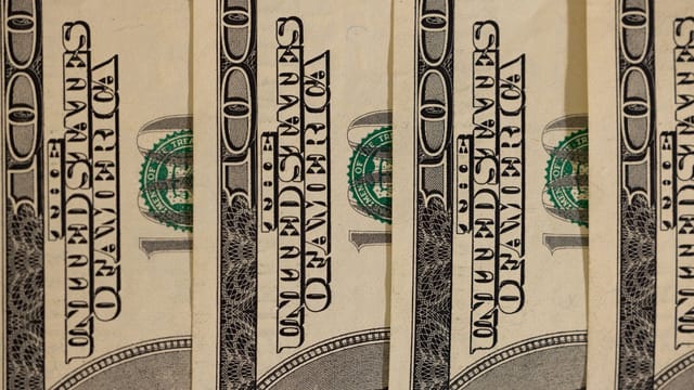 Detailed close-up of multiple US hundred dollar bills, showcasing currency design.
