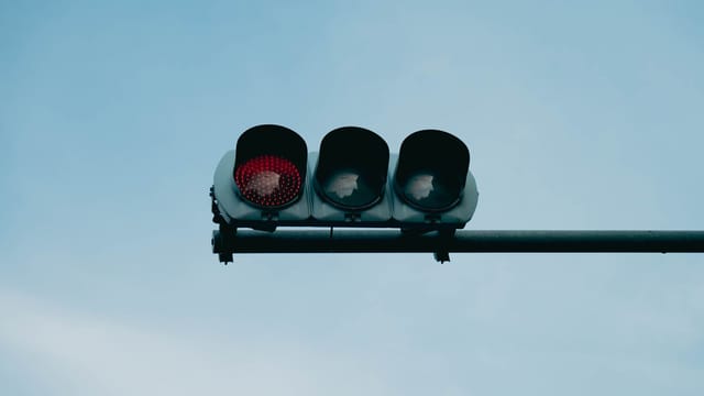 A close-up of a red traffic light set against a clear blue sky, conveying safety and caution.