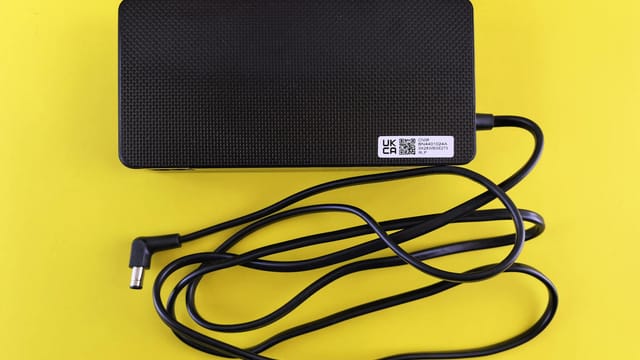 A black power adapter with cord on a vibrant yellow background, showcasing electronics.