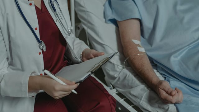 Doctor reviewing medical chart while assisting a patient in a hospital bed.