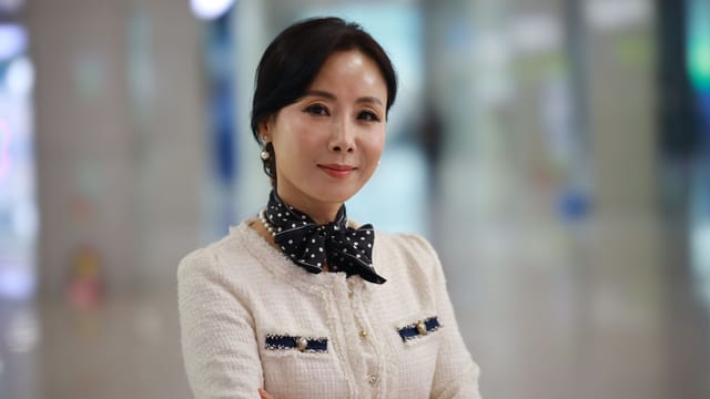 A sophisticated woman smiles confidently in a stylish outfit indoors, exuding elegance and charm.