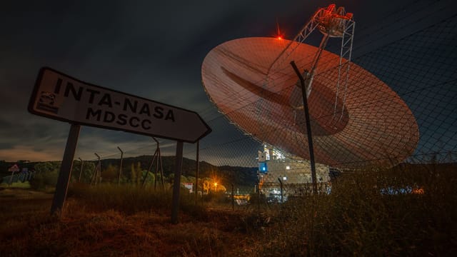 A nighttime view of a satellite dish at Madrid Deep Space Communications Complex under a dark sky.