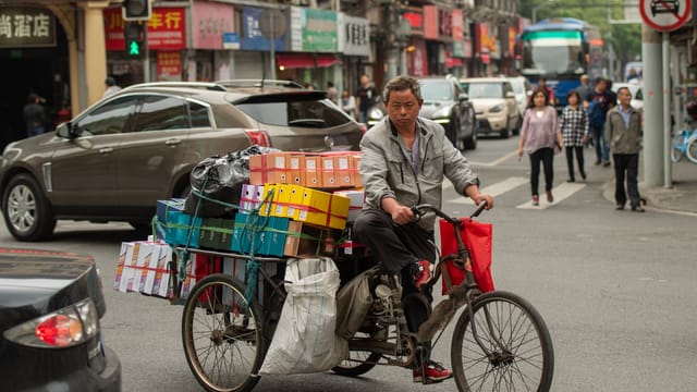 A man transporting goods on a tricycle in a bustling Shanghai street, showcasing urban life and local commerce.