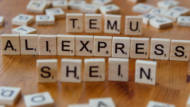 Wooden Scrabble tiles display popular e-commerce platforms on a wooden surface.