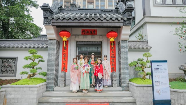A group of people in traditional attire posing at a Chinese temple entrance with decorative red banners.