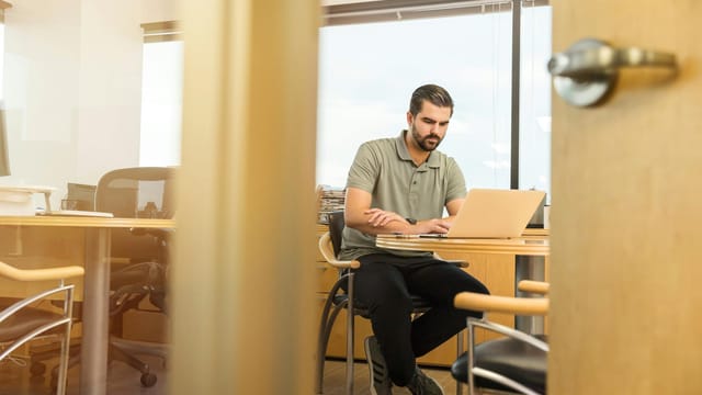 Professional man sitting at desk in modern office, working on laptop.