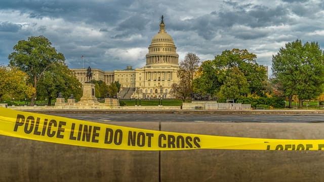 View of US Capitol Building behind police tape under a cloudy sky in Washington, DC.