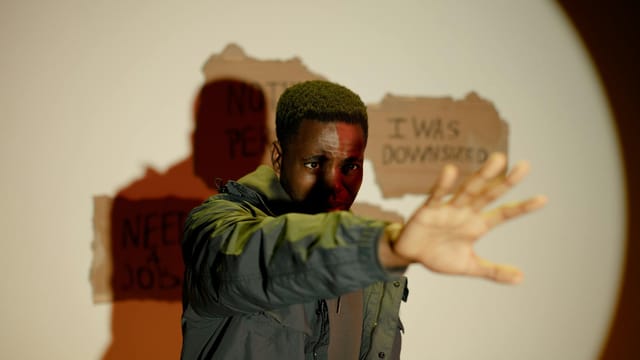 A man stands with an outstretched hand, conveying crisis and unemployment indoors.