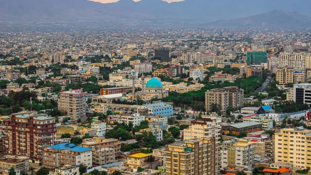 Aerial cityscape of Kabul featuring a prominent mosque amidst modern architecture and mountains.