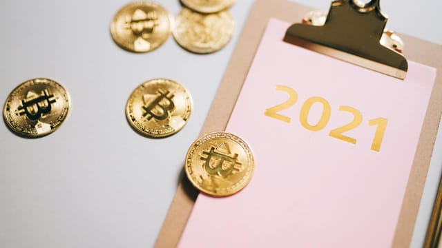 Golden bitcoins scattered around a 2021 clipboard, symbolizing financial planning.