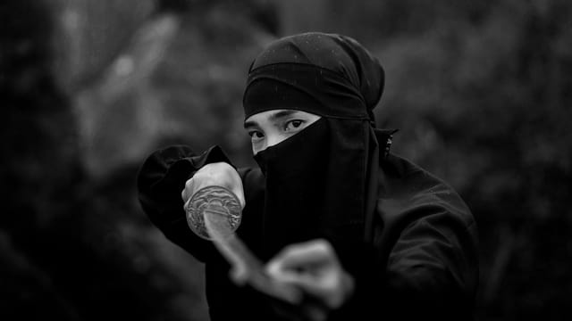 A dramatic black and white photo of a masked samurai warrior wielding a katana, conveying mystery and tradition.