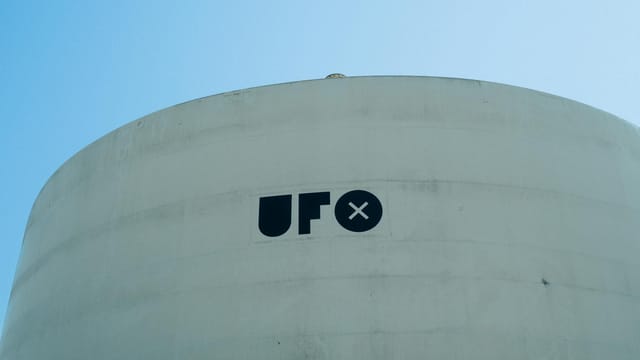 Minimalist image of a white cylindrical structure with 'UFO' text under a clear blue sky.