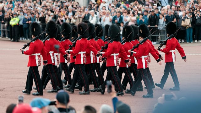 Changing of the Guard ceremony at Buckingham Palace, London, featuring soldiers in traditional red uniforms.