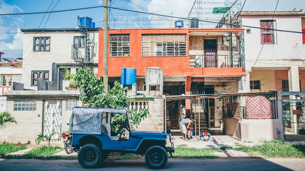 Vibrant street view in Havana with vintage blue jeep and urban architecture.