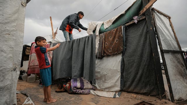 Children in a Gaza Strip refugee camp construct a makeshift shelter. A poignant scene of resilience.