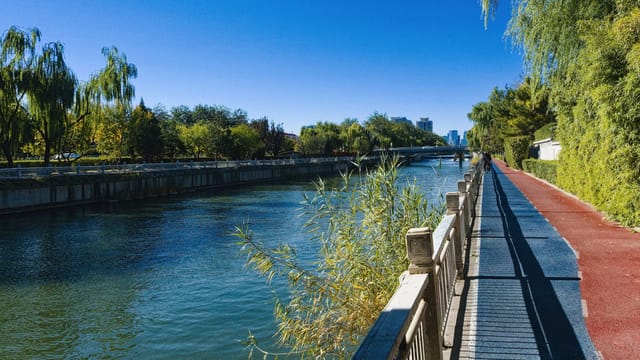 Serene riverside path lined with trees under a clear blue sky in Beijing, China, perfect for leisure walks.
