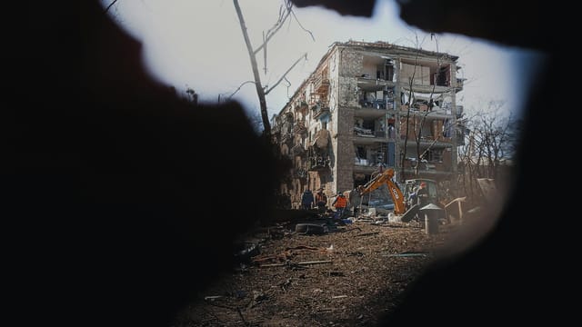 A damaged building in Kyiv, Ukraine, with surrounding destruction and machinery, showcasing urban conflict aftermath.