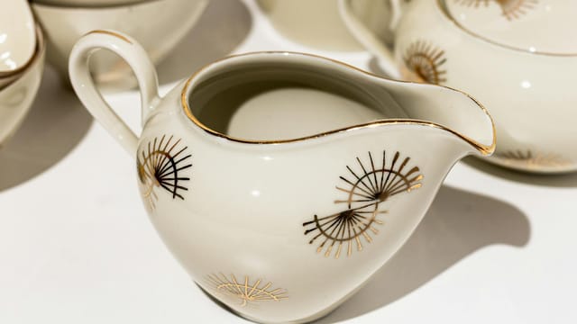 Close-up of a white ceramic creamer featuring a gold decorative pattern. Perfect for tea or coffee settings.