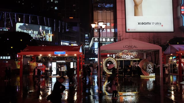 Lively night market scene in a bustling city with illuminated billboards and people.