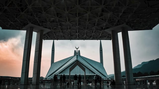 A stunning view of Faisal Mosque during twilight in Islamabad, showcasing Islamic architecture with silhouetted visitors.