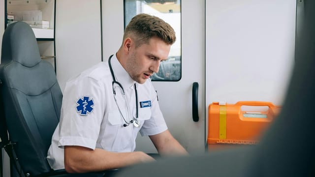 Focused paramedic in an ambulance setting, wearing uniform and stethoscope, ready for emergency response.