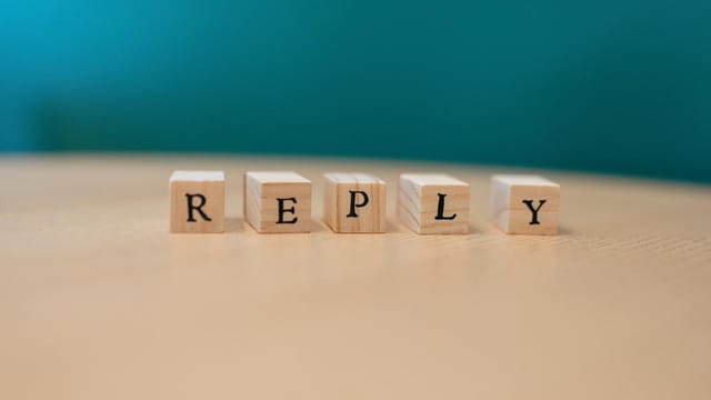 Close-up of wooden blocks spelling 'REPLY' on a table with teal background.