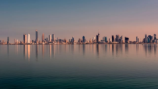 Beautiful Kuwait City skyline reflected on calm water at sunset, showcasing modern architecture.