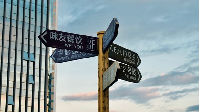 Direction signs in urban area with skyscraper backdrop at sunset.