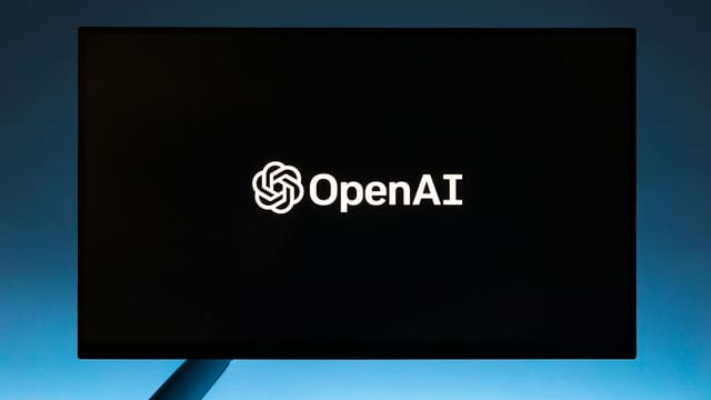 Minimalist display of OpenAI logo on a screen, set against a gradient blue background.