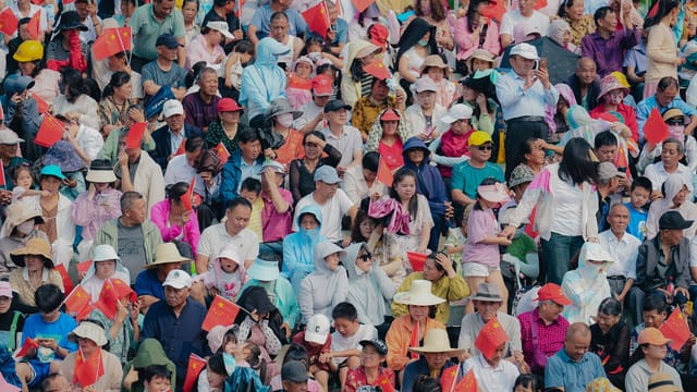 A densely packed crowd with flowers and flags fills a vibrant stadium, exuding excitement.