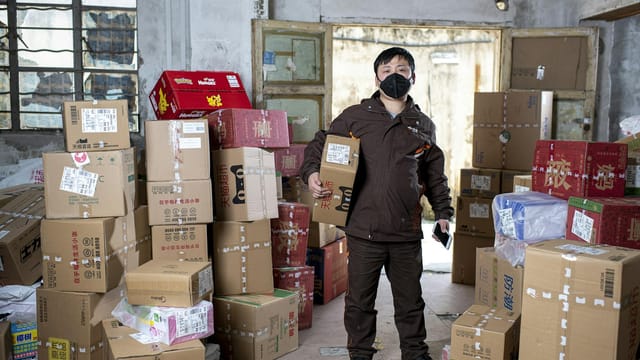 Delivery worker holding packages in a Wuhan warehouse, wearing a face mask.