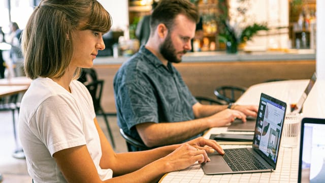 Two young professionals working on laptops in a modern cafe setting.