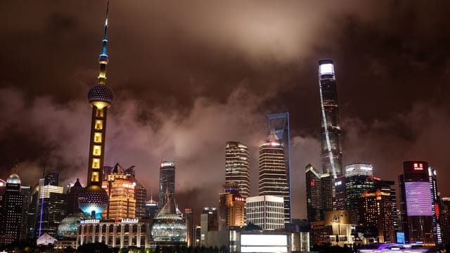 Dramatic nighttime view of Shanghai's skyline with the iconic Oriental Pearl Tower illuminated against a cloudy sky.