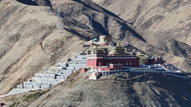 Stunning aerial view of a Tibetan monastery nestled on a rugged mountain landscape.