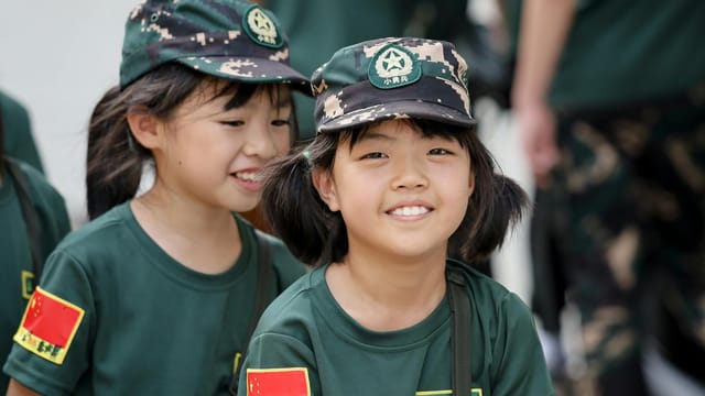 Smiling children wearing camouflage uniforms with Chinese flags, showcasing youthful friendship.